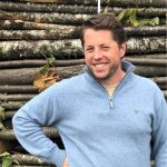 Fast Solutions - Een man in een blauwe trui die voor een stapel boomstammen staat en zijn ervaring met Fast Solutions-David demonstreert.